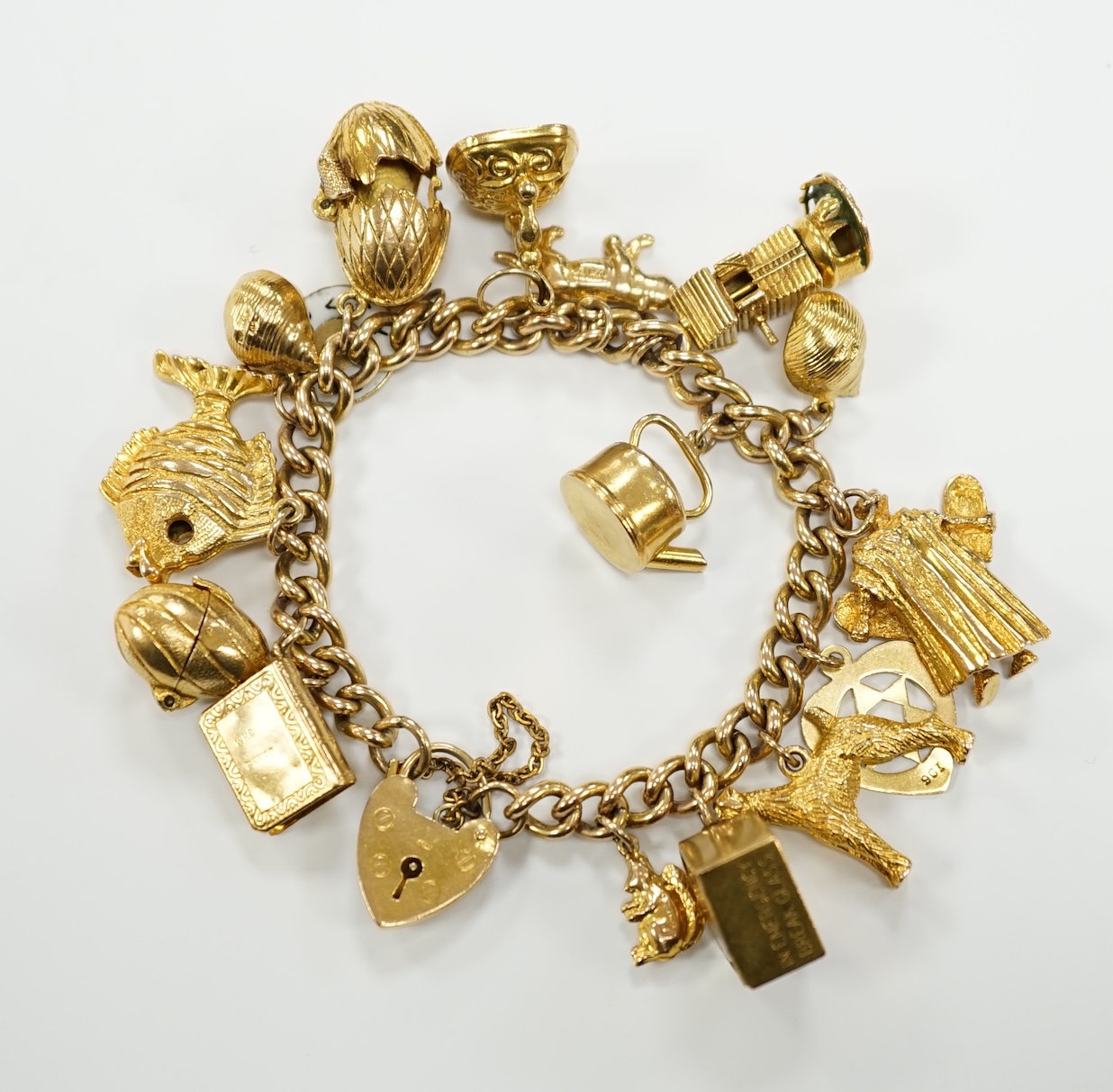 A 9ct gold curb link charm bracelet, with heart shaped padlock clasp and hung with assorted mainly 9ct gold charms